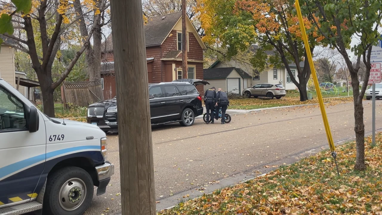 A child on an electric bike at a crosswalk in a residential neighborhood, with a truck in the background.